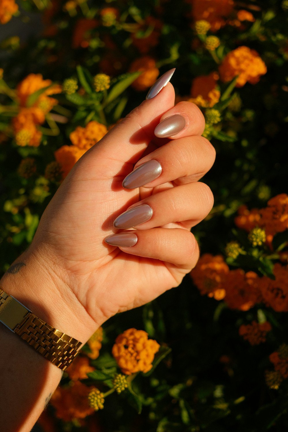 Almond nails in a soft metallic nude against marigolds